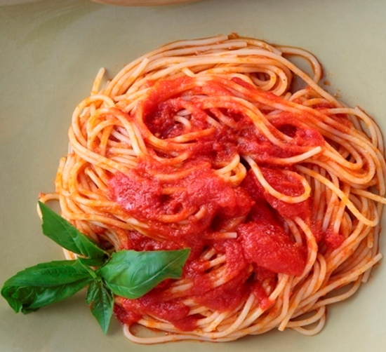 白い器に盛り付けられたトマトソースのパスタと添えられたバジルの写真
