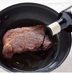 ステーキ肉にバルサミコ酢をかけている調理写真