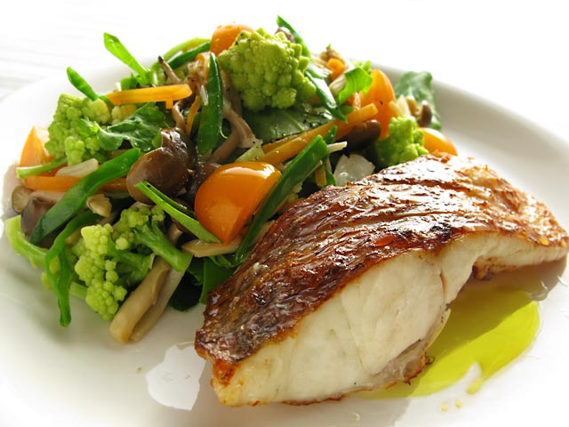 丸皿に盛りつけられた白身魚のグリルと野菜の料理写真