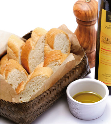 カゴに入った薄切りのフランスパンのとなりにオリーブオイルの瓶、ソルトミル、小皿に注がれたオリーブオイルが並んでいる写真